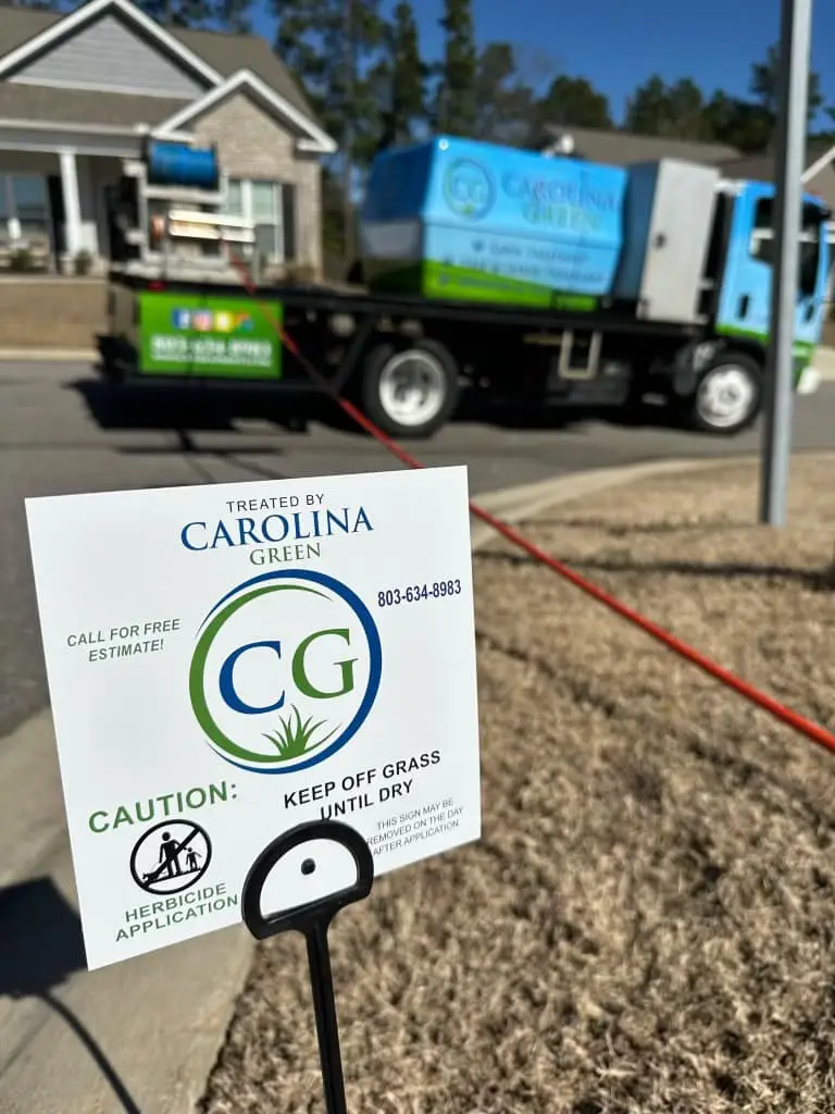 A Carolina Green Treatments yard sign on a freshly treated lawn, the spray truck behind it